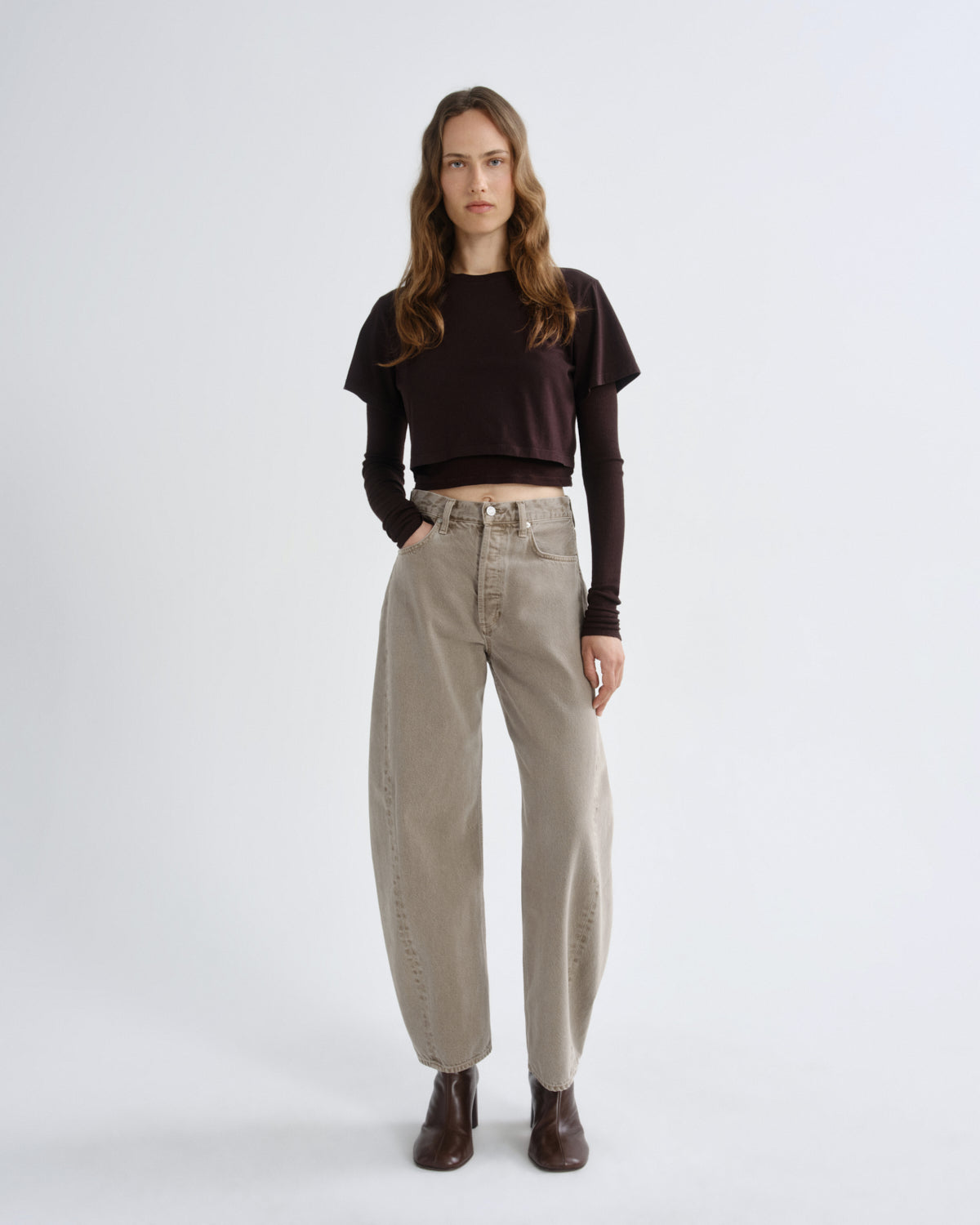 Woman wearing a brown sweater and beige pants on a white background
