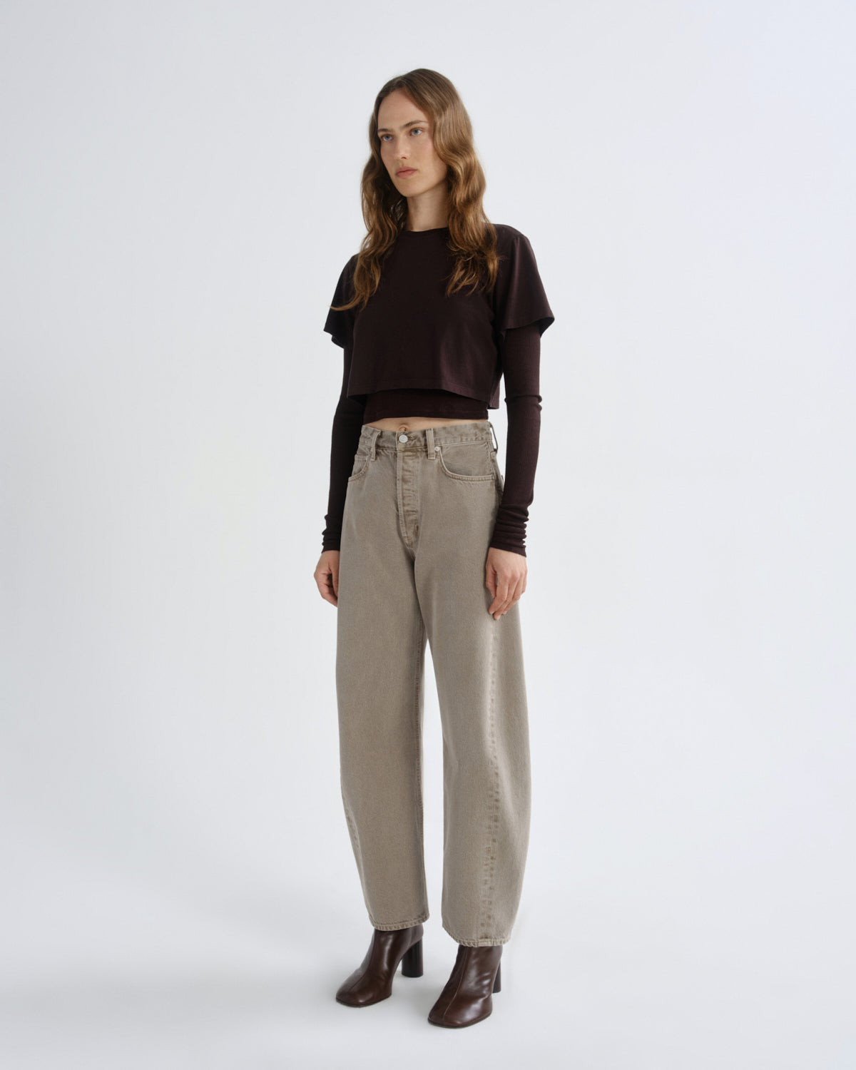 Woman wearing a brown cropped top and beige high-waisted jeans on a white background