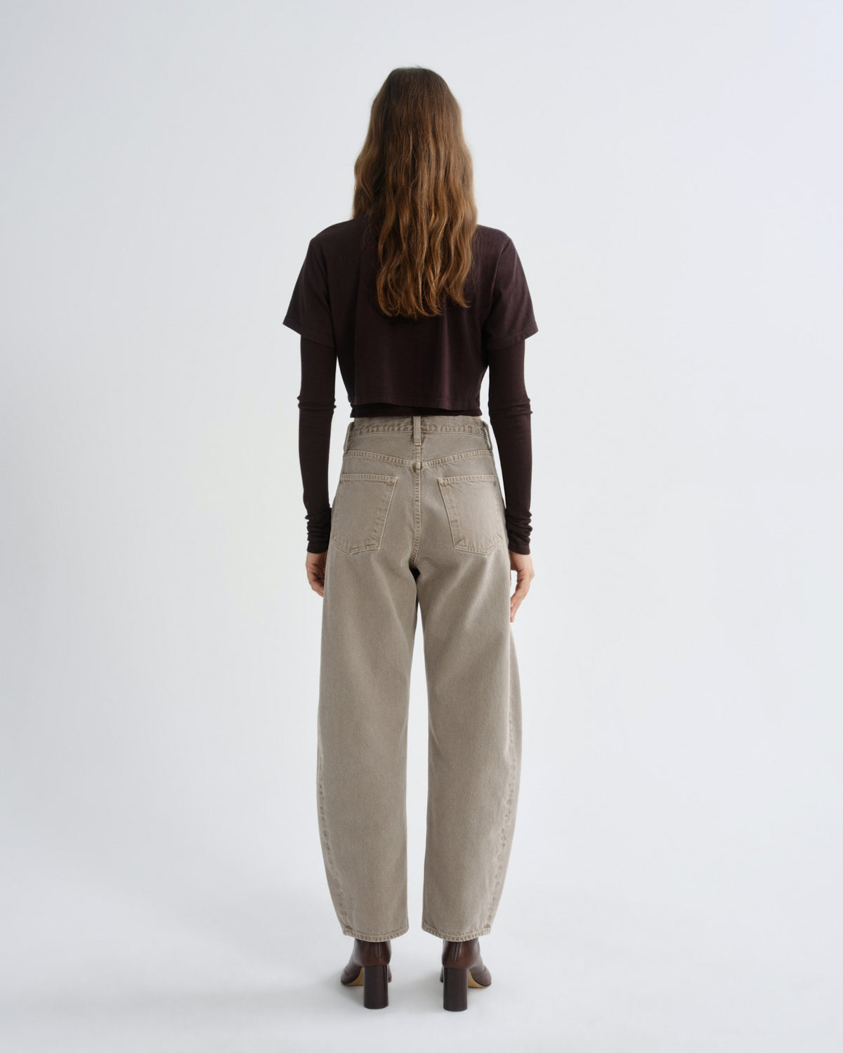 Person wearing beige pants and a brown top on a white background