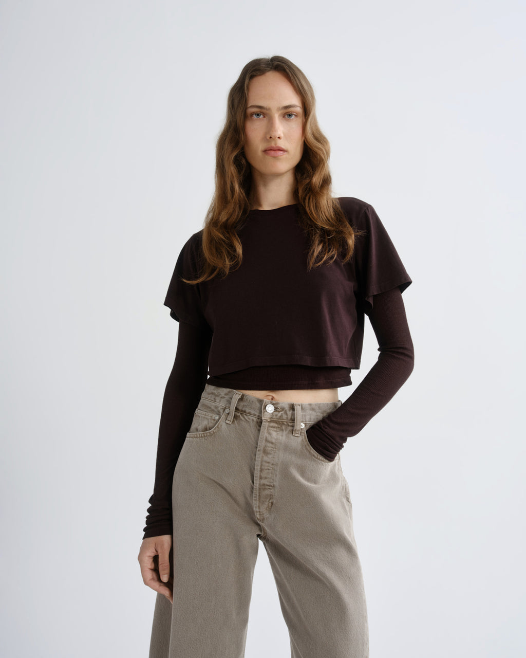 Woman wearing a dark brown ruffled top and beige pants on a white background