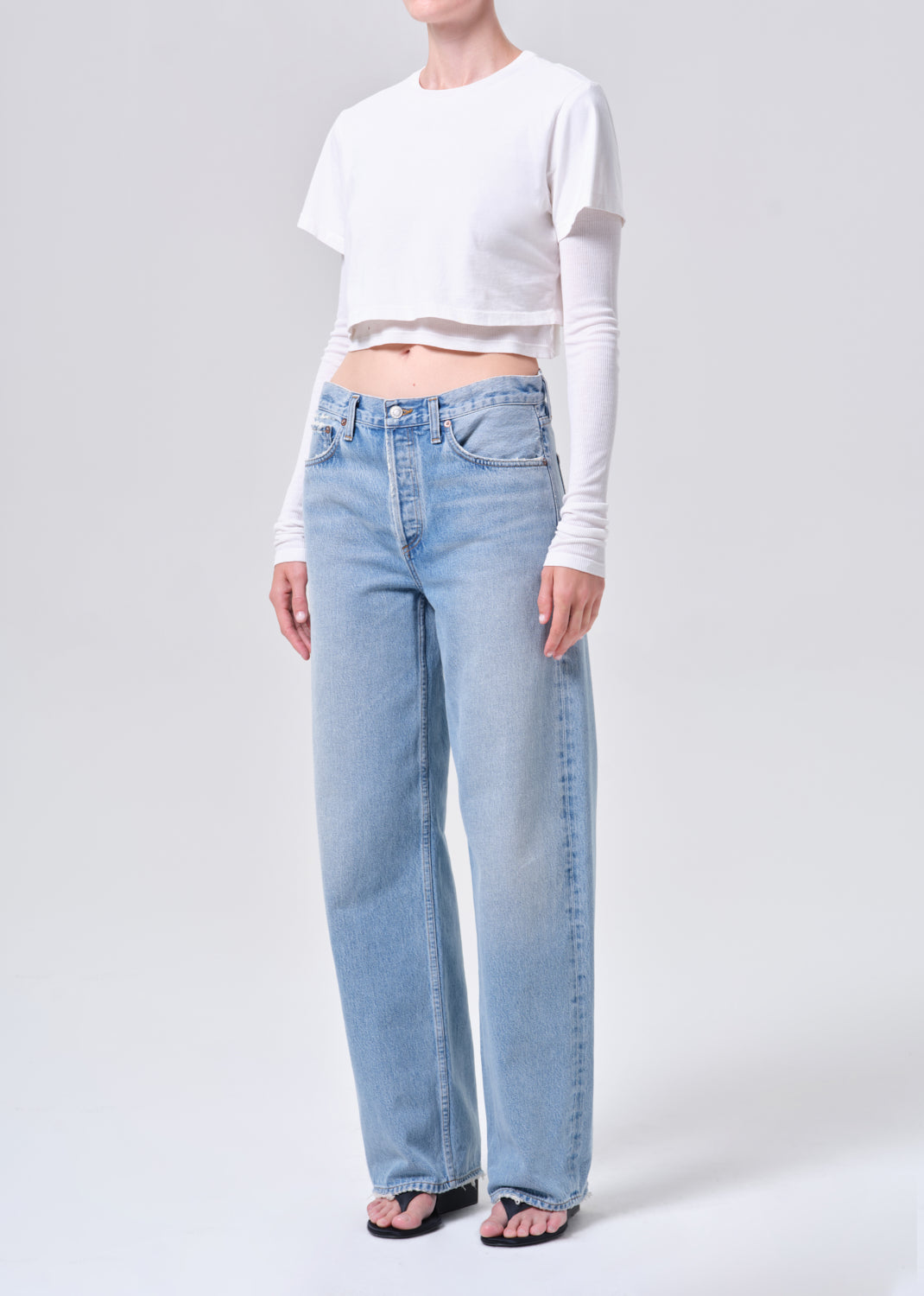 Person wearing light blue jeans and a white cropped top on a plain background