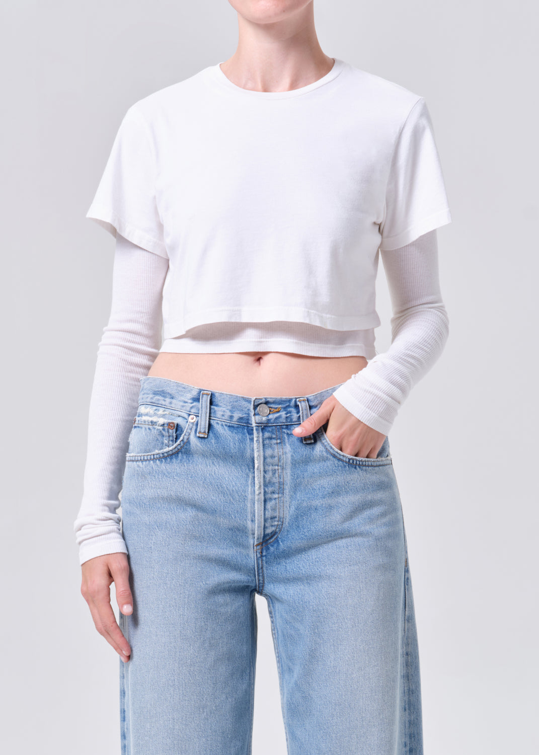 Person wearing a white cropped t-shirt and light blue jeans on a gray background