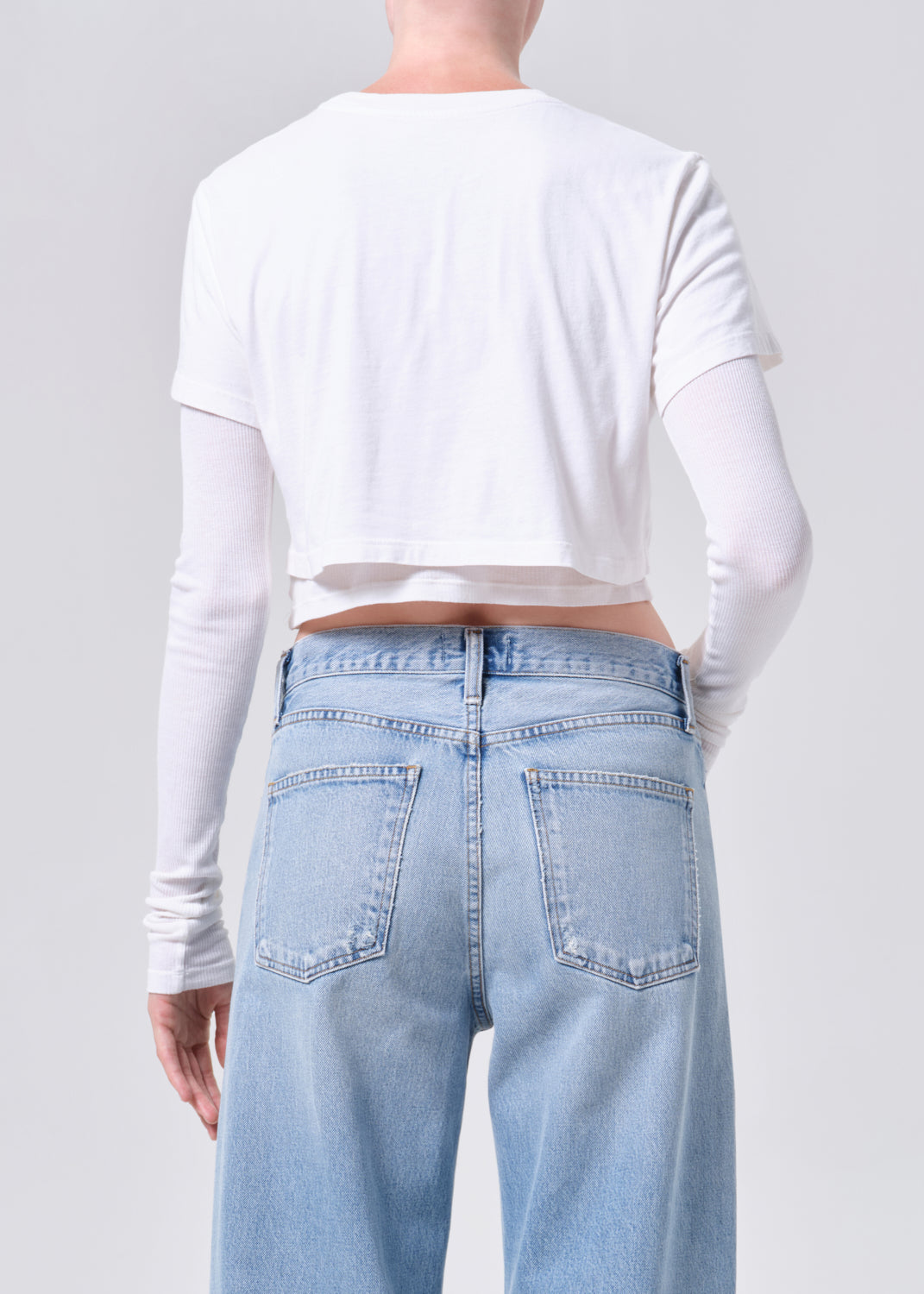 Person wearing a white long-sleeve crop top and light blue jeans on a plain background