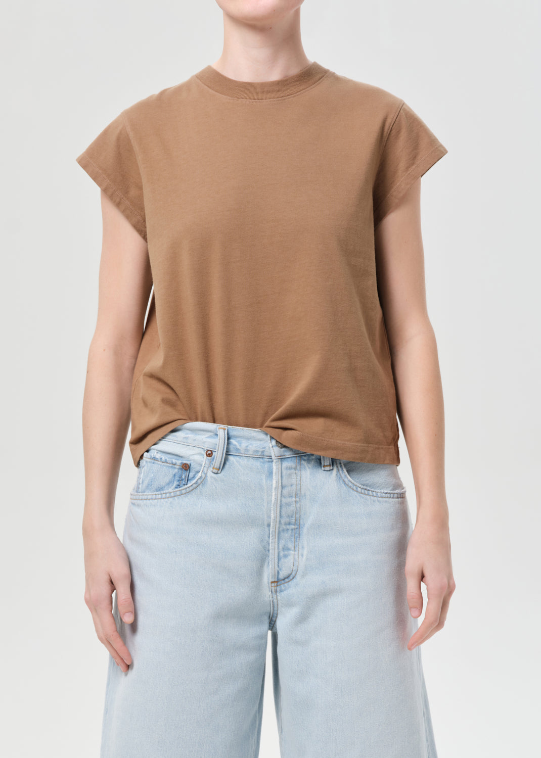 Person wearing a brown t-shirt and light blue jeans on a plain background