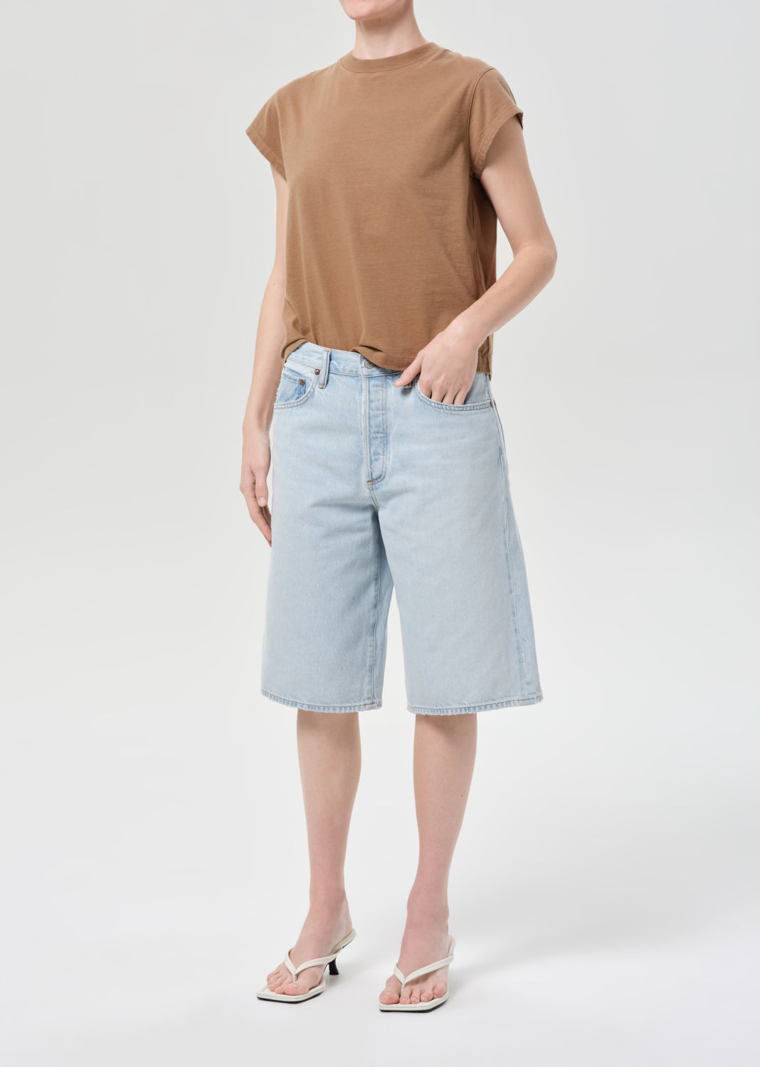 Person wearing a brown t-shirt and light blue denim shorts on a white background