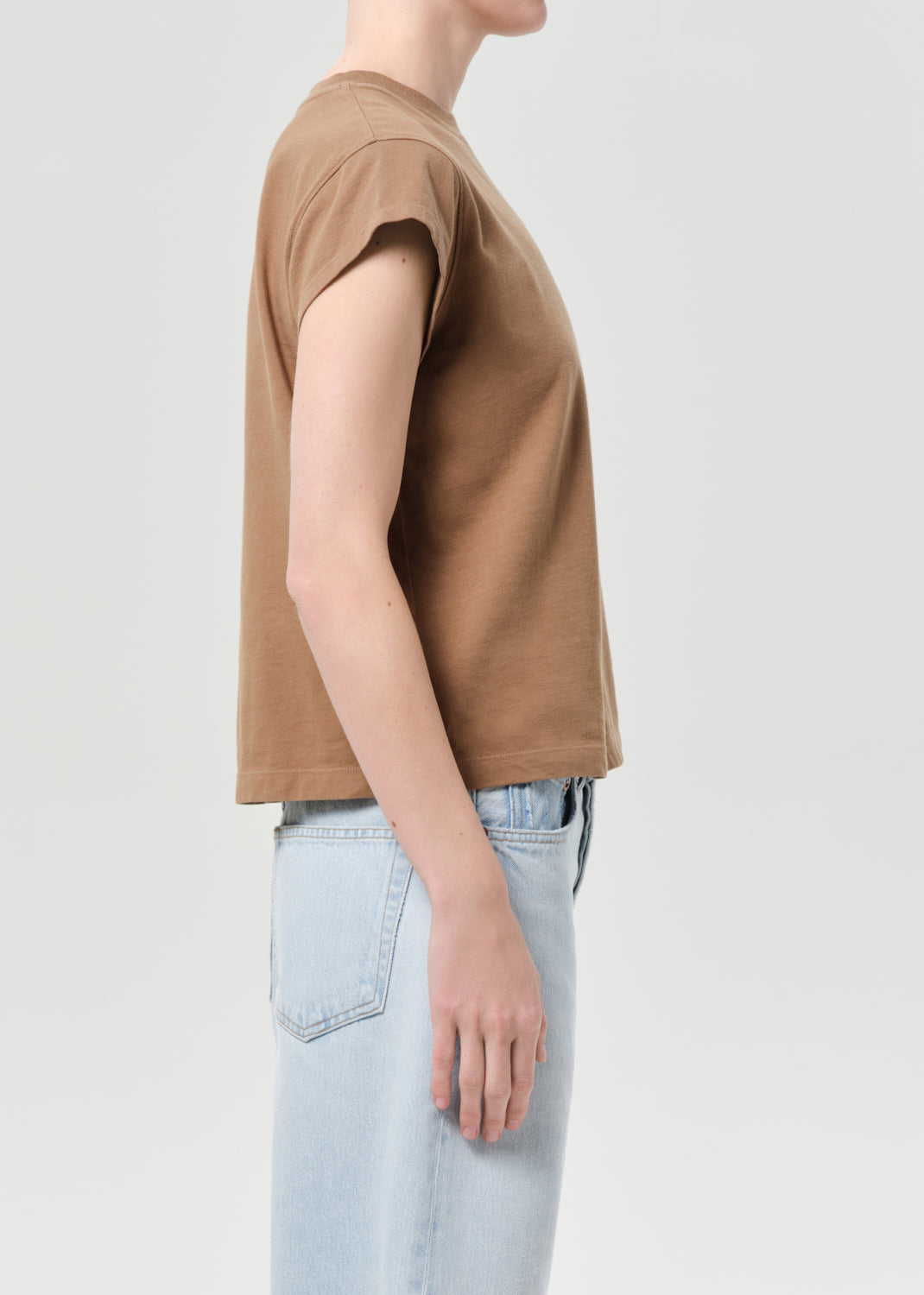 Person wearing a brown t-shirt and light blue jeans on a plain background