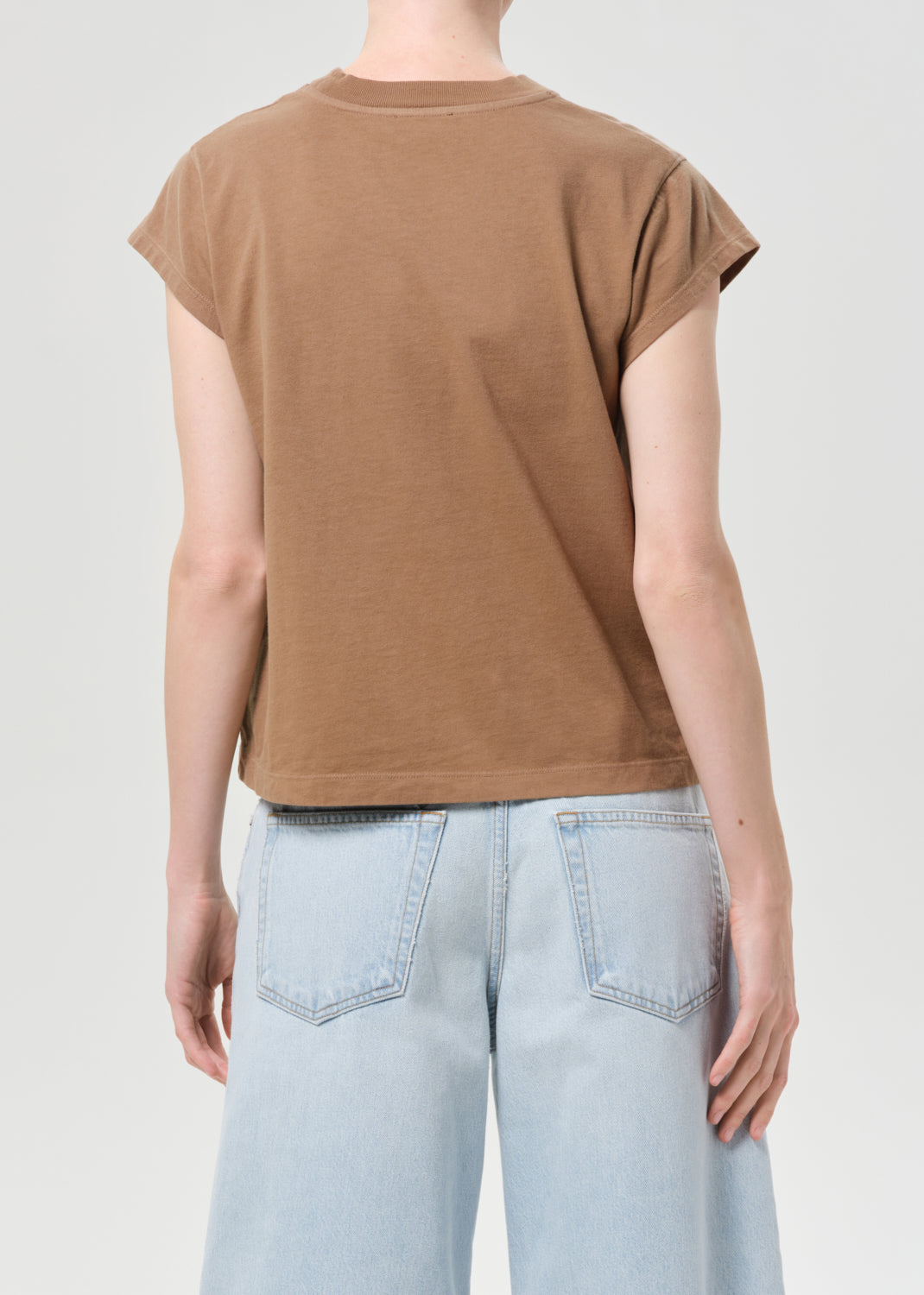 Person wearing a brown t-shirt and light blue jeans on a plain background