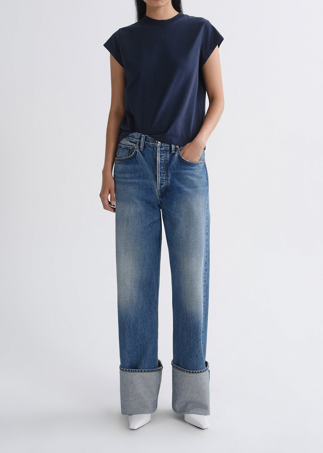 A model wearing a navy blue short-sleeve t-shirt and wide-leg blue jeans with rolled cuffs, standing against a grey background.