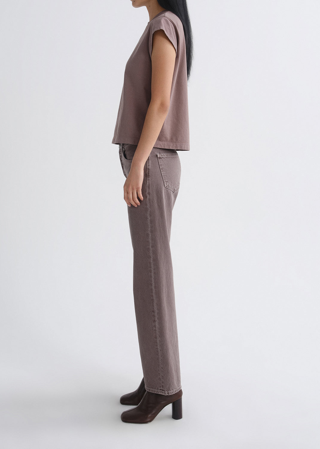 Person wearing a mauve cap sleeve tee with mauve straight leg jeans viewed from the side on a grey background