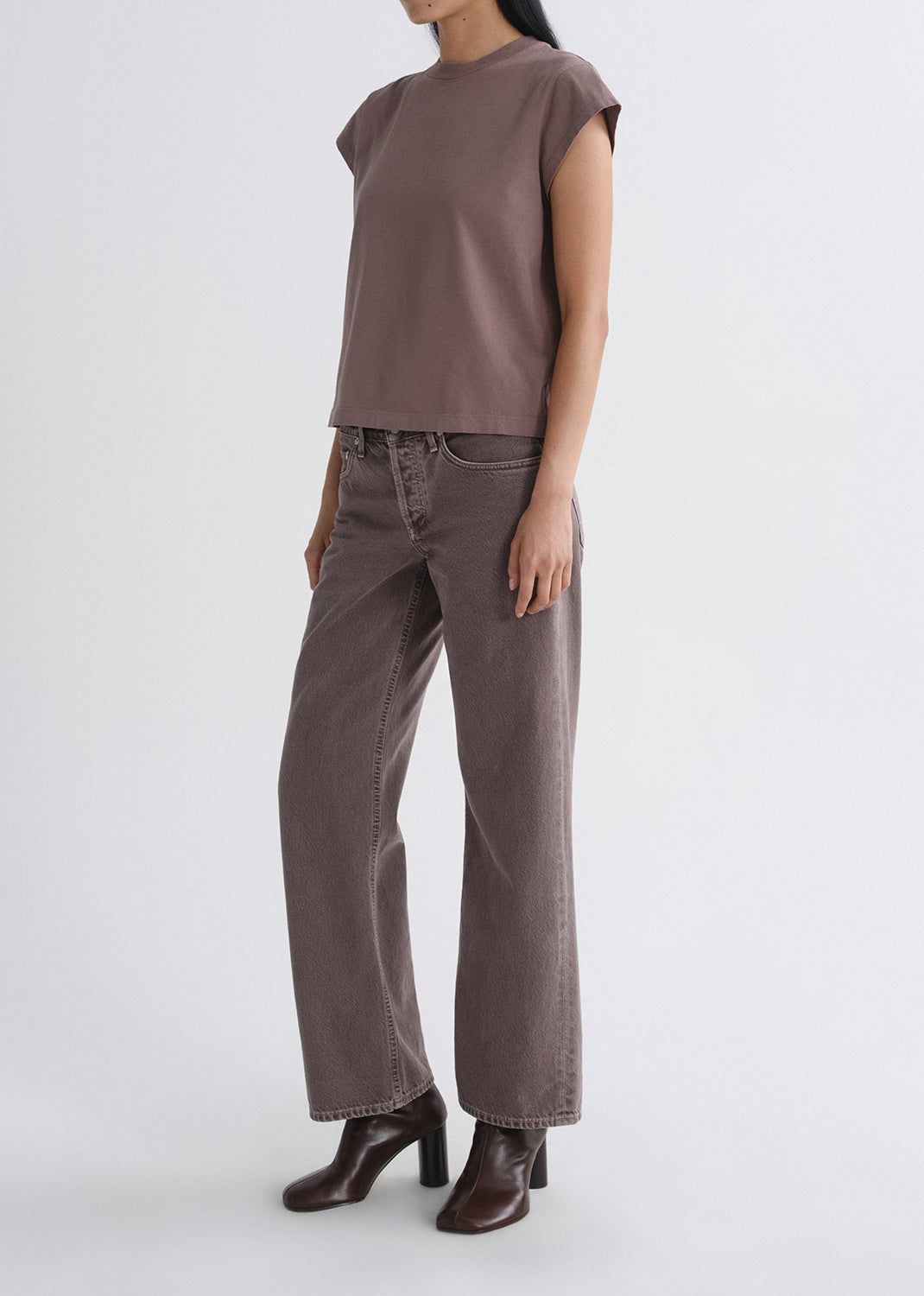 Person wearing a mauve cap sleeve tee with mauve straight leg jeans on a grey background