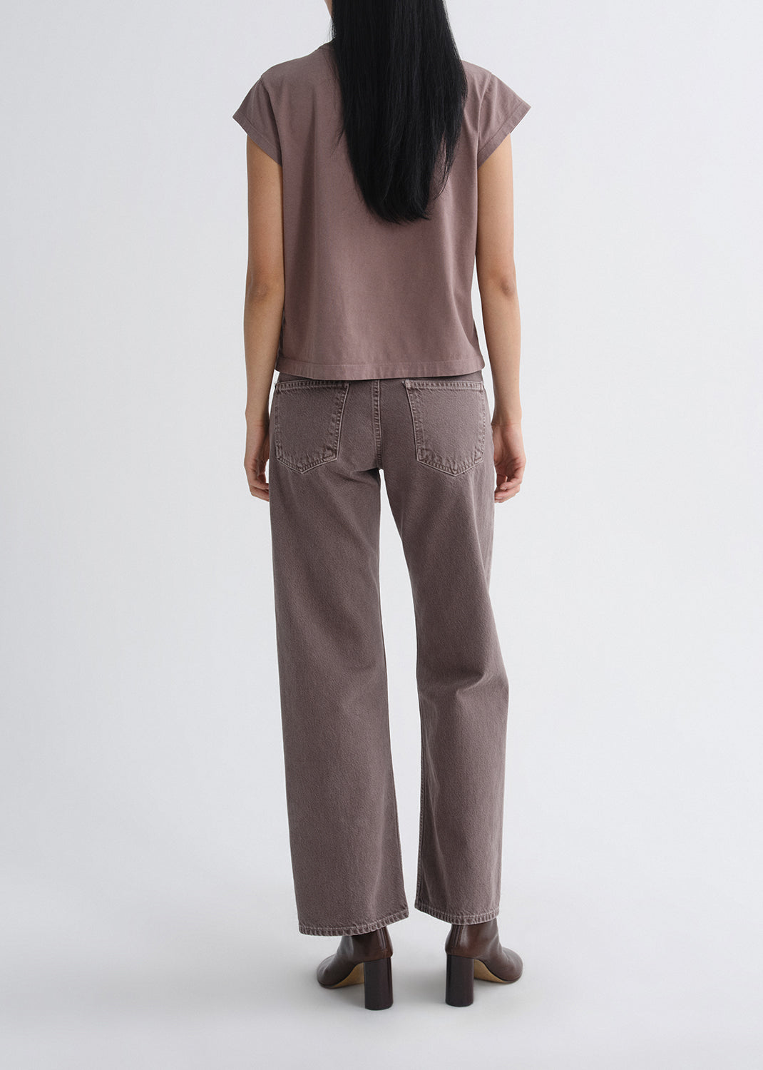 Person wearing a mauve cap sleeve tee with mauve straight leg jeans viewed from the back on a grey background