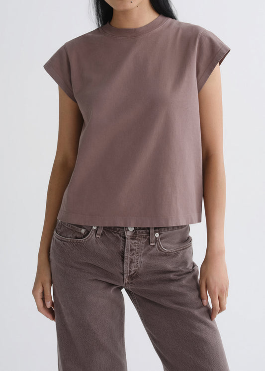Person wearing a mauve cap sleeve tee on a grey background