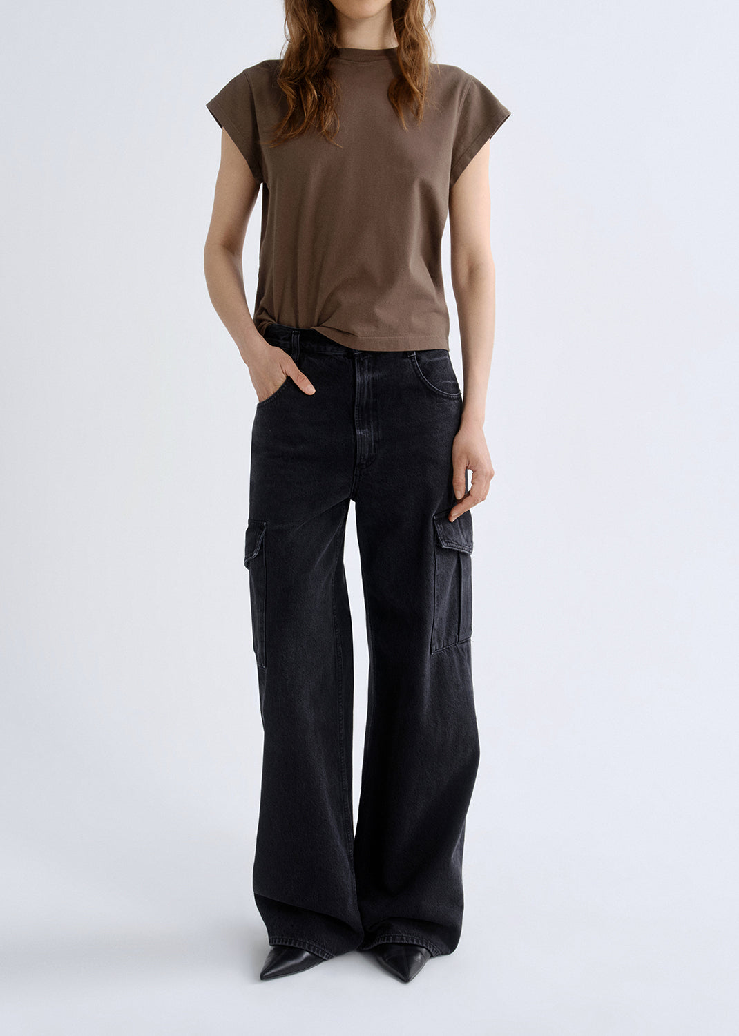 Person wearing a brown t-shirt and black cargo pants on a grey background