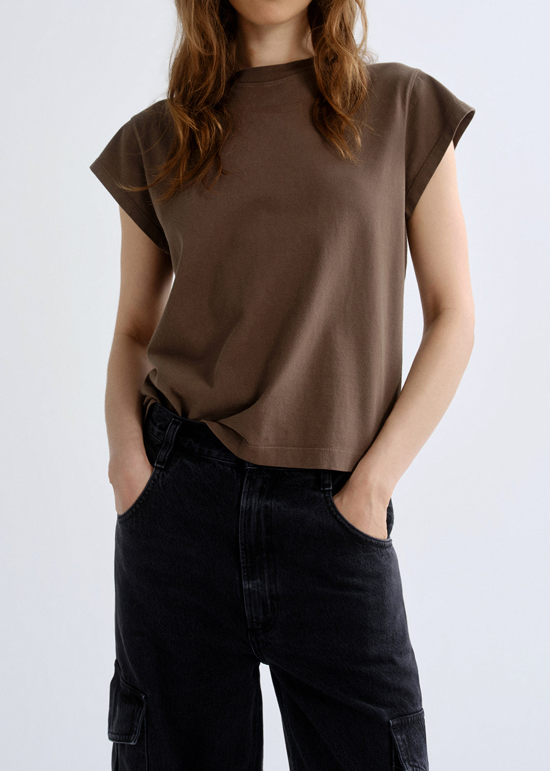 Person wearing a brown t-shirt and black pants on a grey background