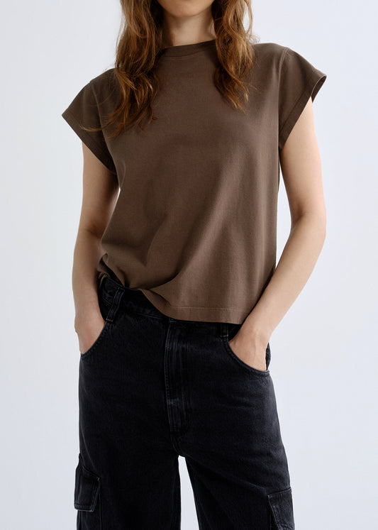 Person wearing a brown t-shirt and black pants on a grey background