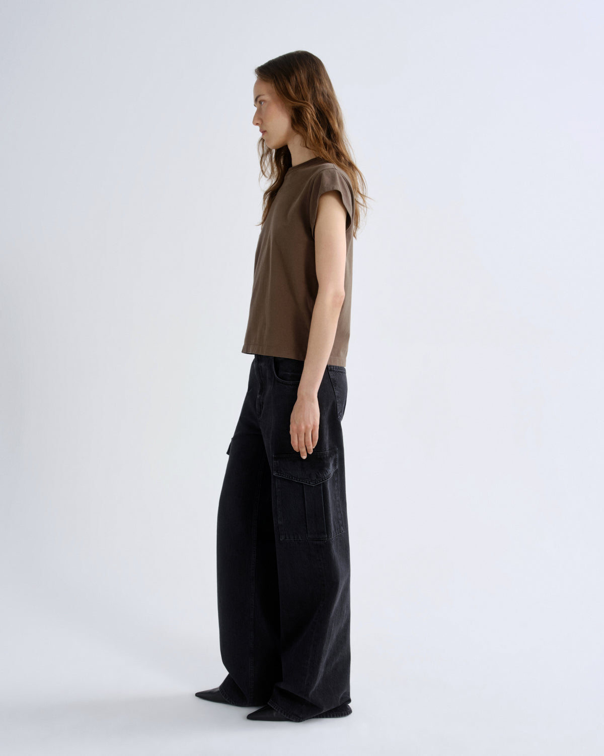 Woman wearing a brown sleeveless top and black cargo pants on a white background