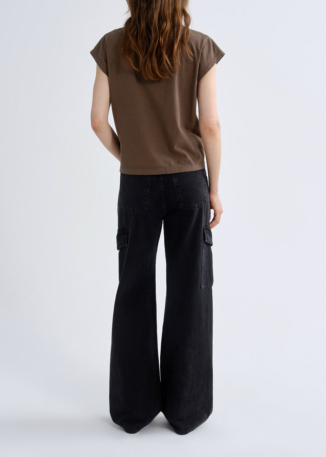 Person wearing a brown top and black cargo pants on a grey background