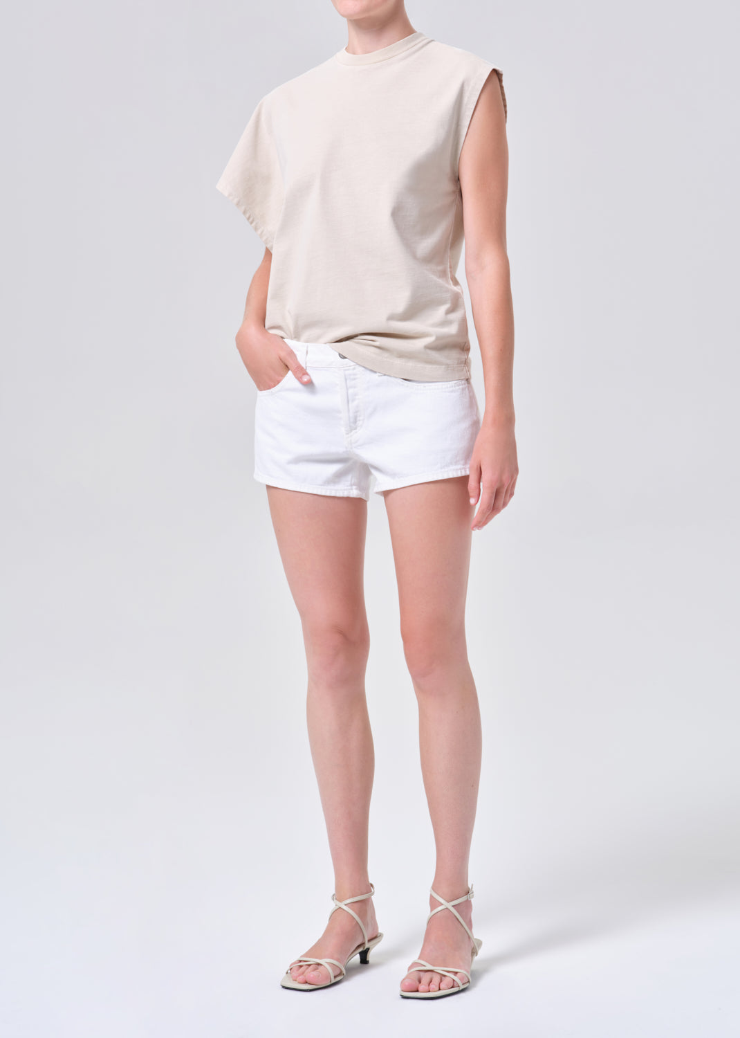 Person wearing a beige sleeveless top and white shorts on a plain background