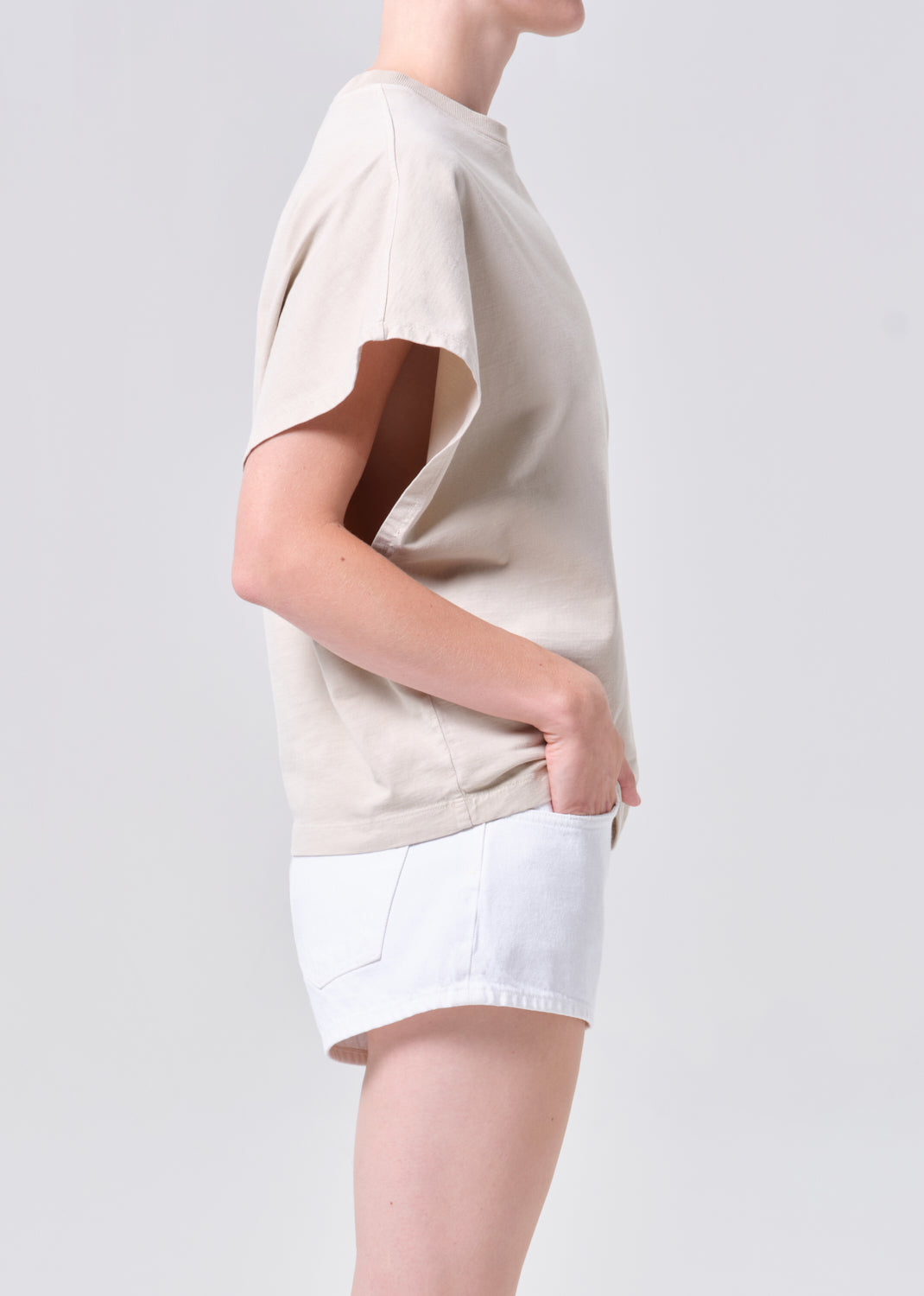 Person wearing a beige t-shirt and white shorts on a plain background