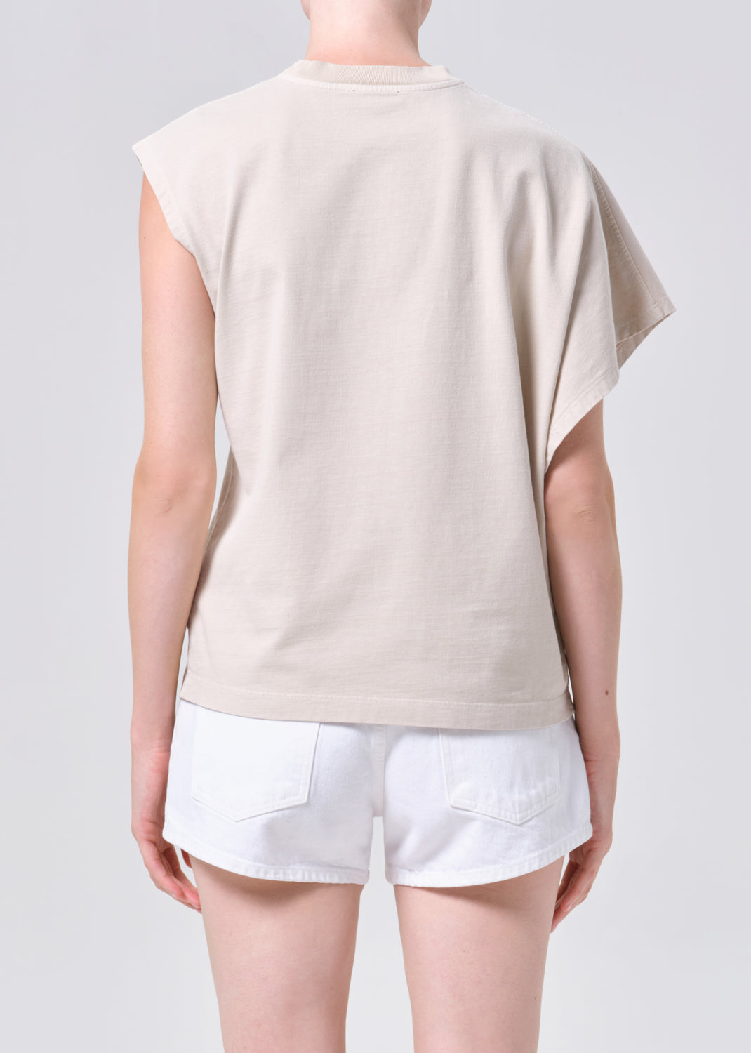 Person wearing a beige sleeveless top and white shorts on a plain background