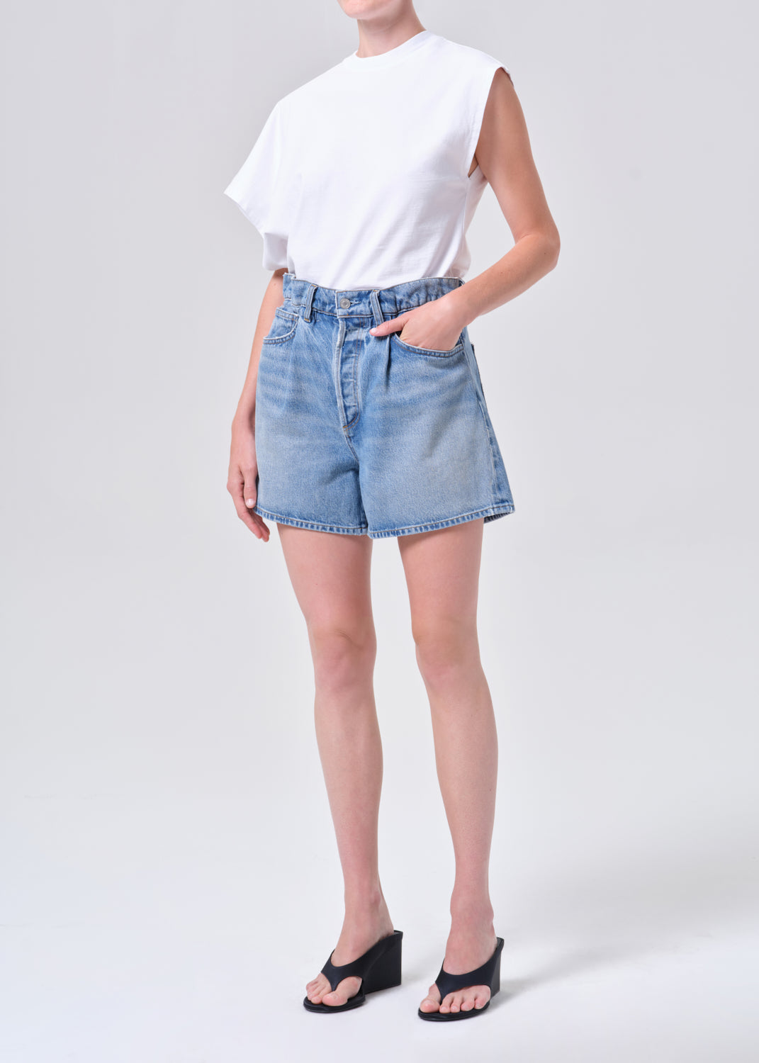 Person wearing a white top and blue denim shorts on a light gray background