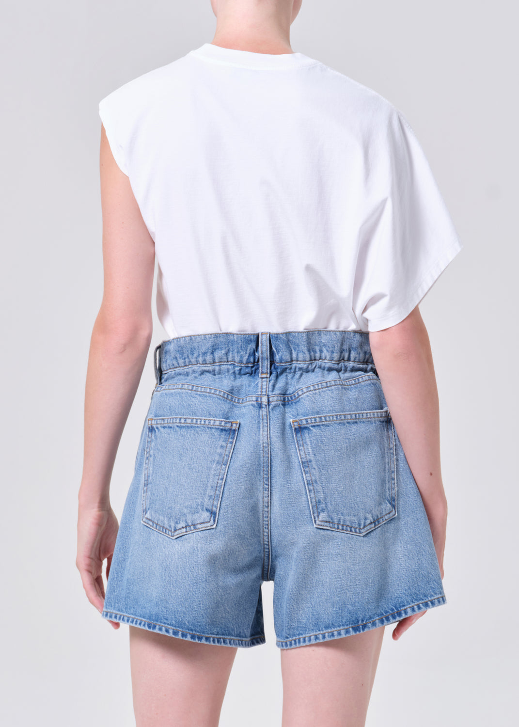 Person wearing a white t-shirt and blue denim shorts on a plain background