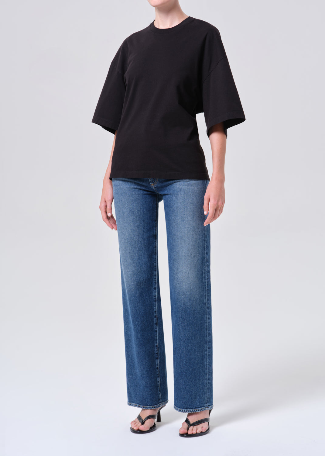 Person wearing a black oversized t-shirt and blue jeans on a white background