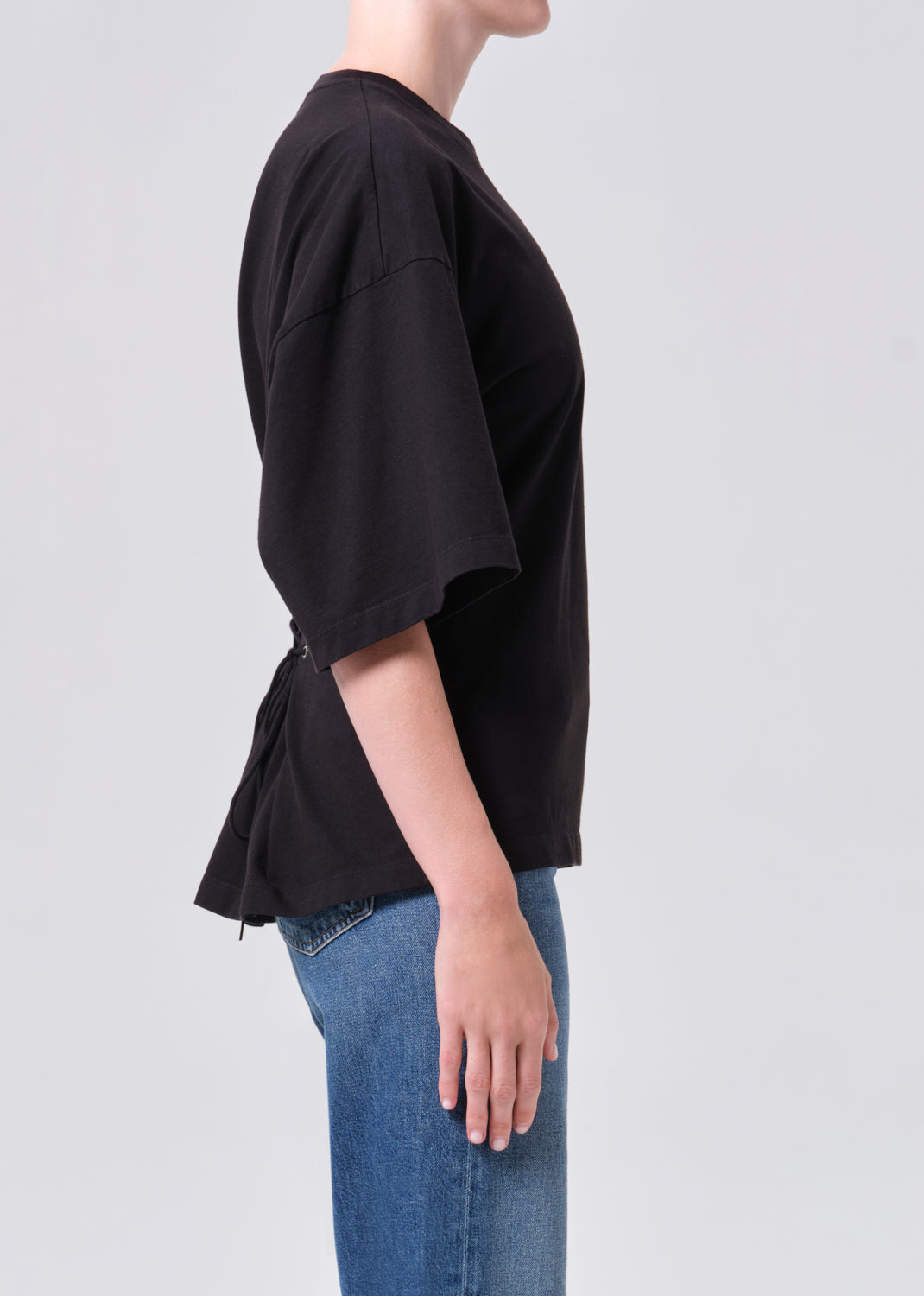 Person wearing a black oversized shirt and blue jeans on a light gray background