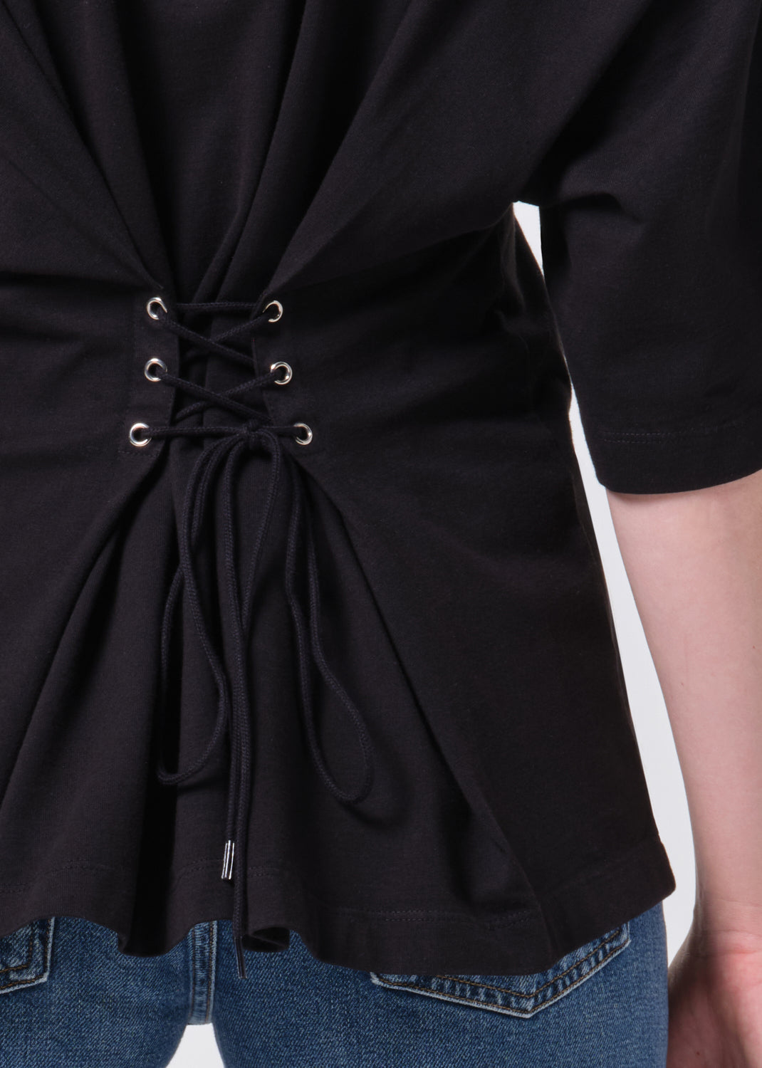 Black top with lace-up front detail worn by a person, on a plain background