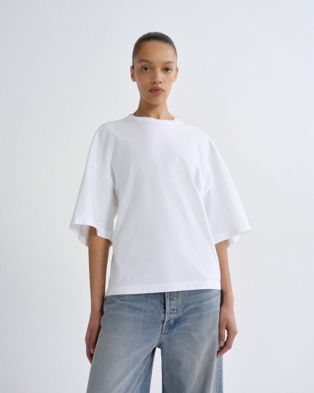 Person wearing a white oversized t-shirt and light blue jeans on a plain background