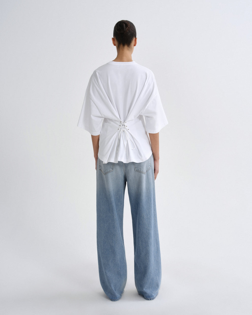 Person wearing a white top and light blue jeans on a plain background