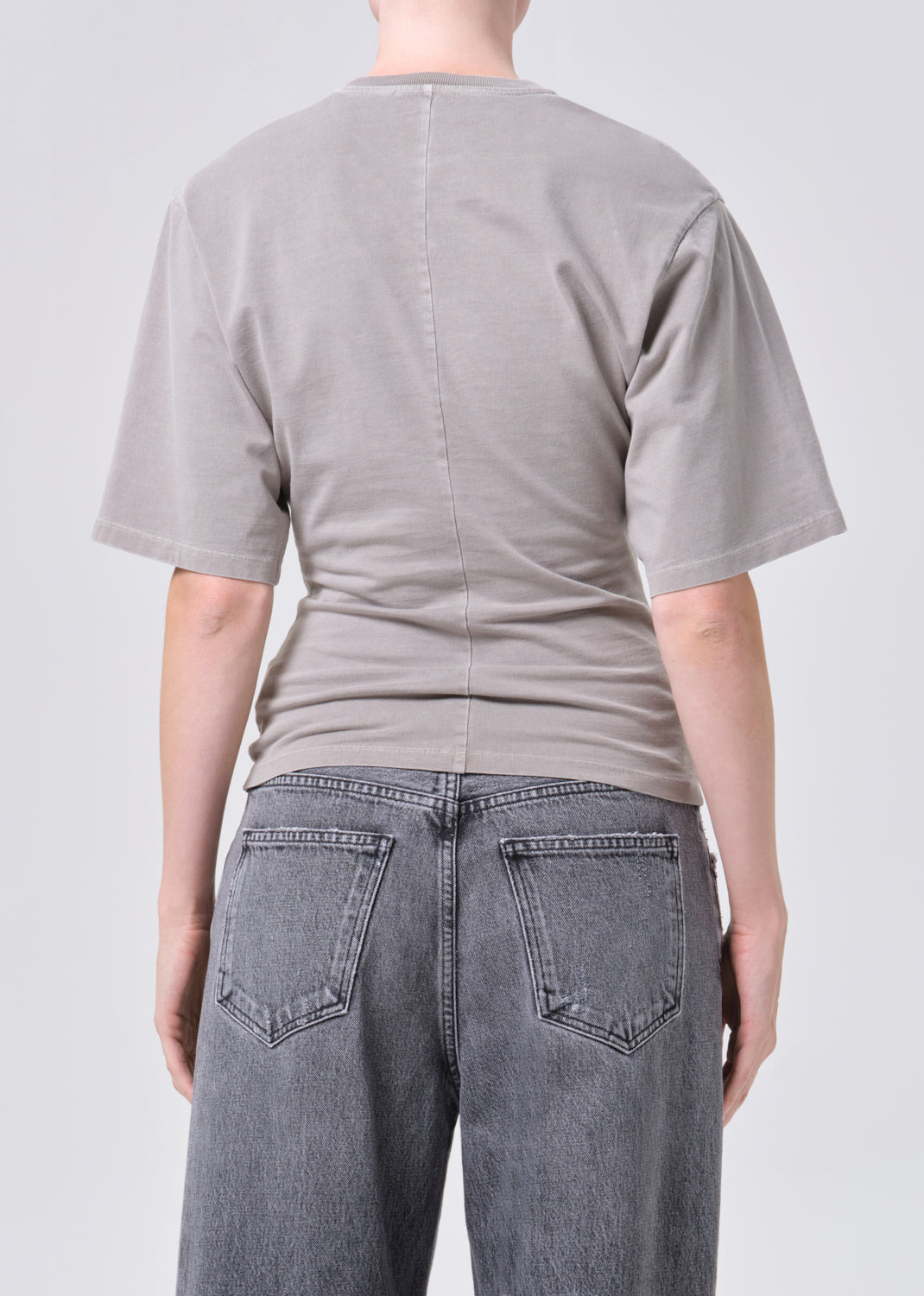 Person wearing a plain gray t-shirt and dark jeans on a light gray background