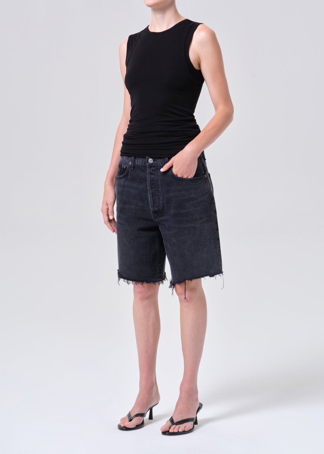 Person wearing a black sleeveless top and denim shorts on a white background