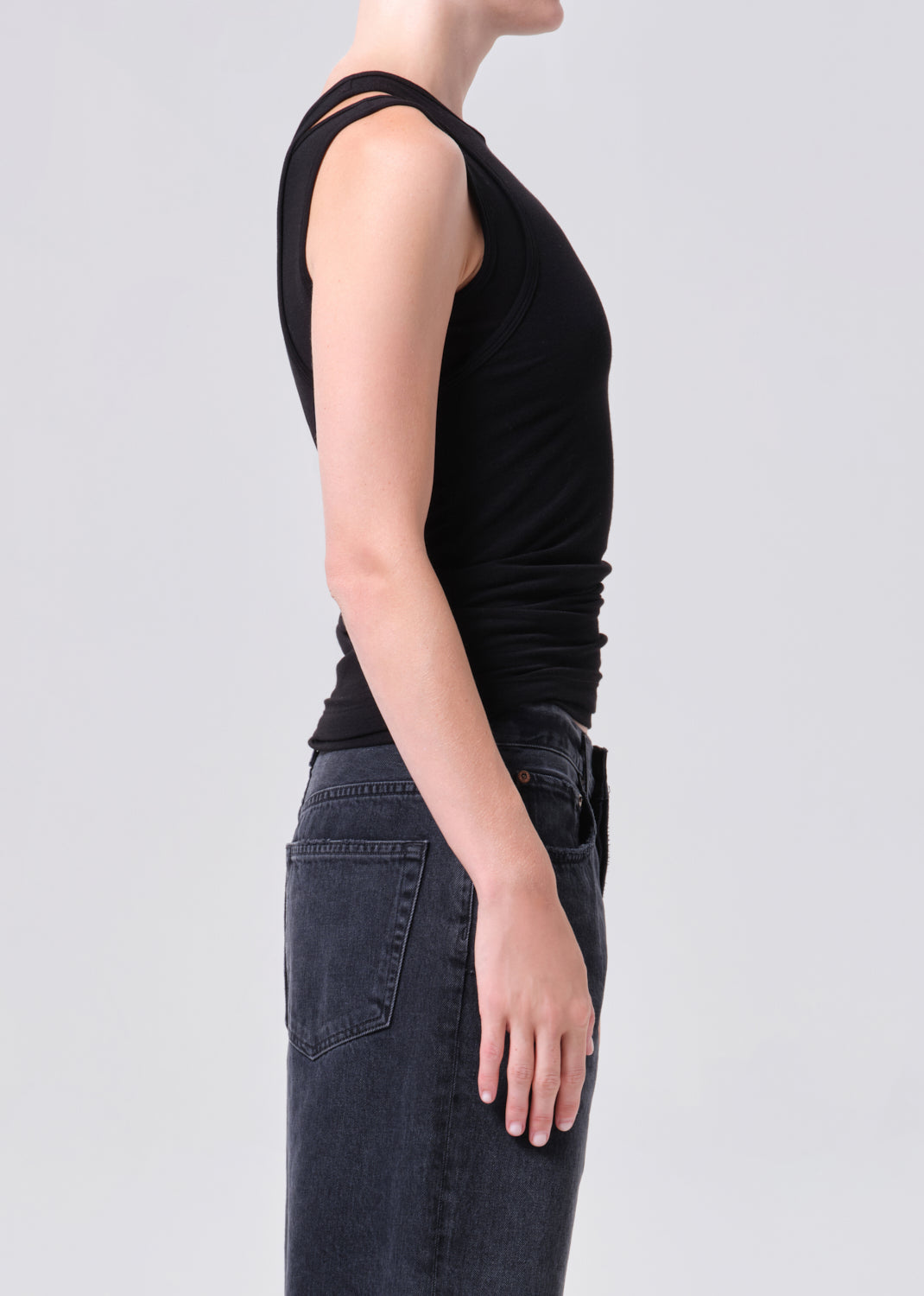 Person wearing a black sleeveless top and dark jeans on a light gray background