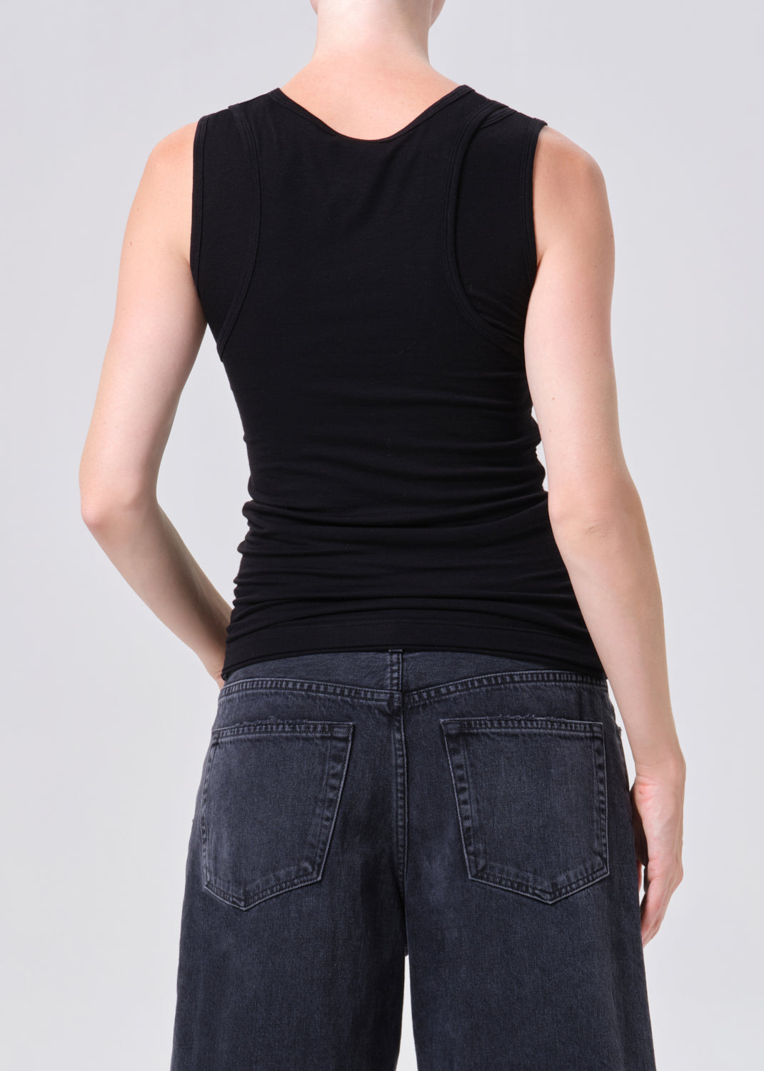 Person wearing a black sleeveless top and dark jeans on a plain background
