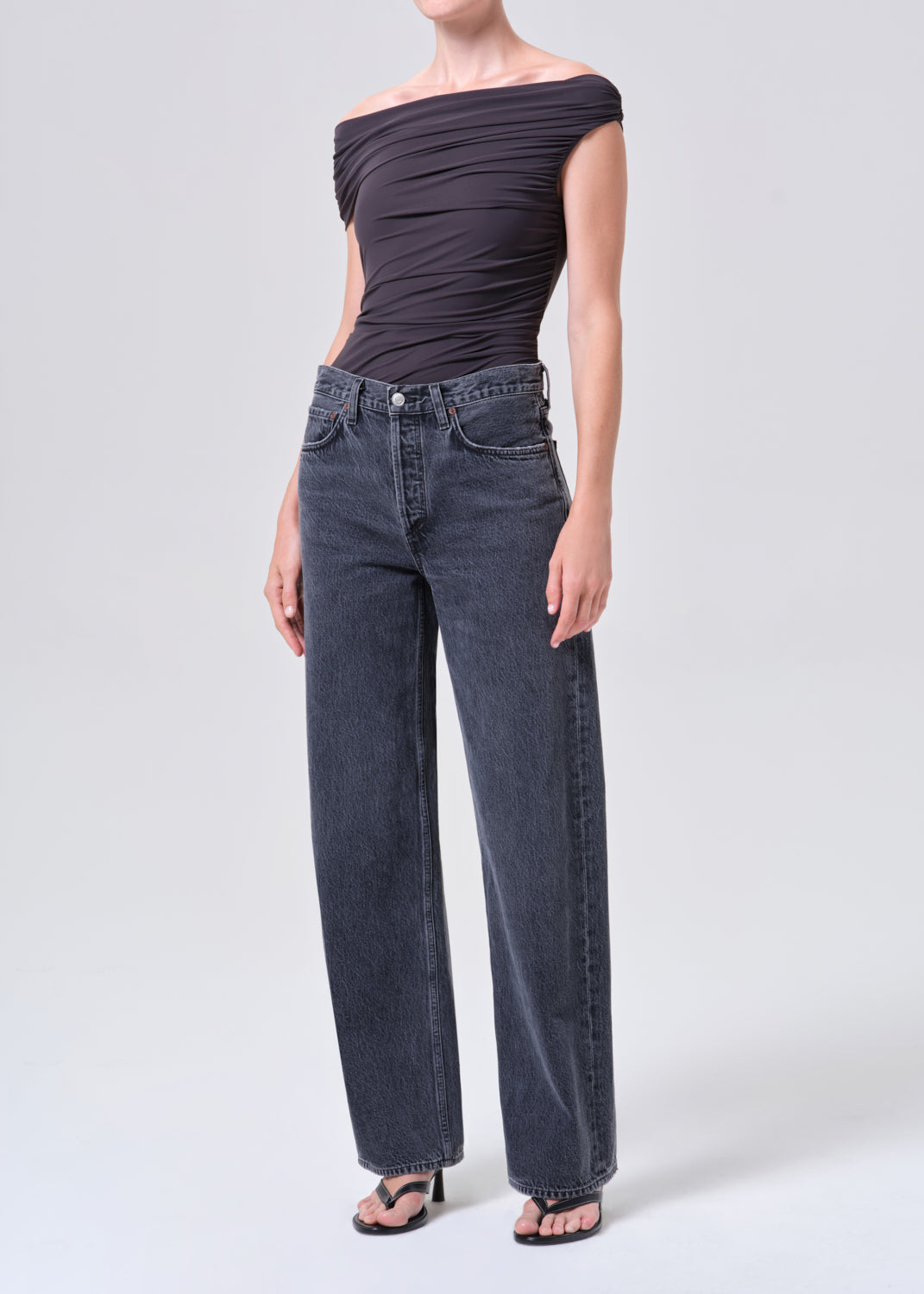 Person wearing a dark gray off-shoulder top and wide-leg jeans on a white background