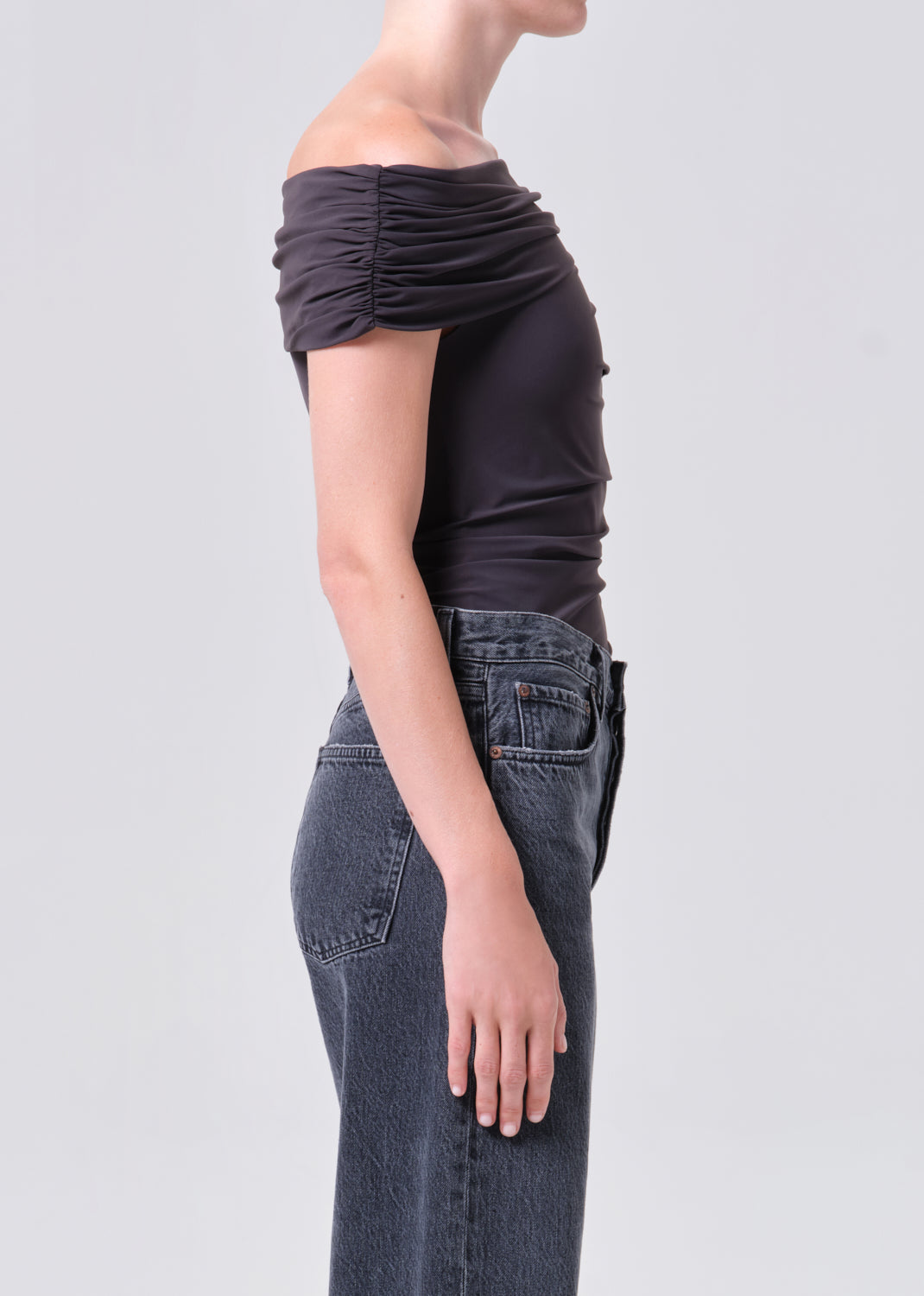 Person wearing a black top and gray jeans on a light gray background