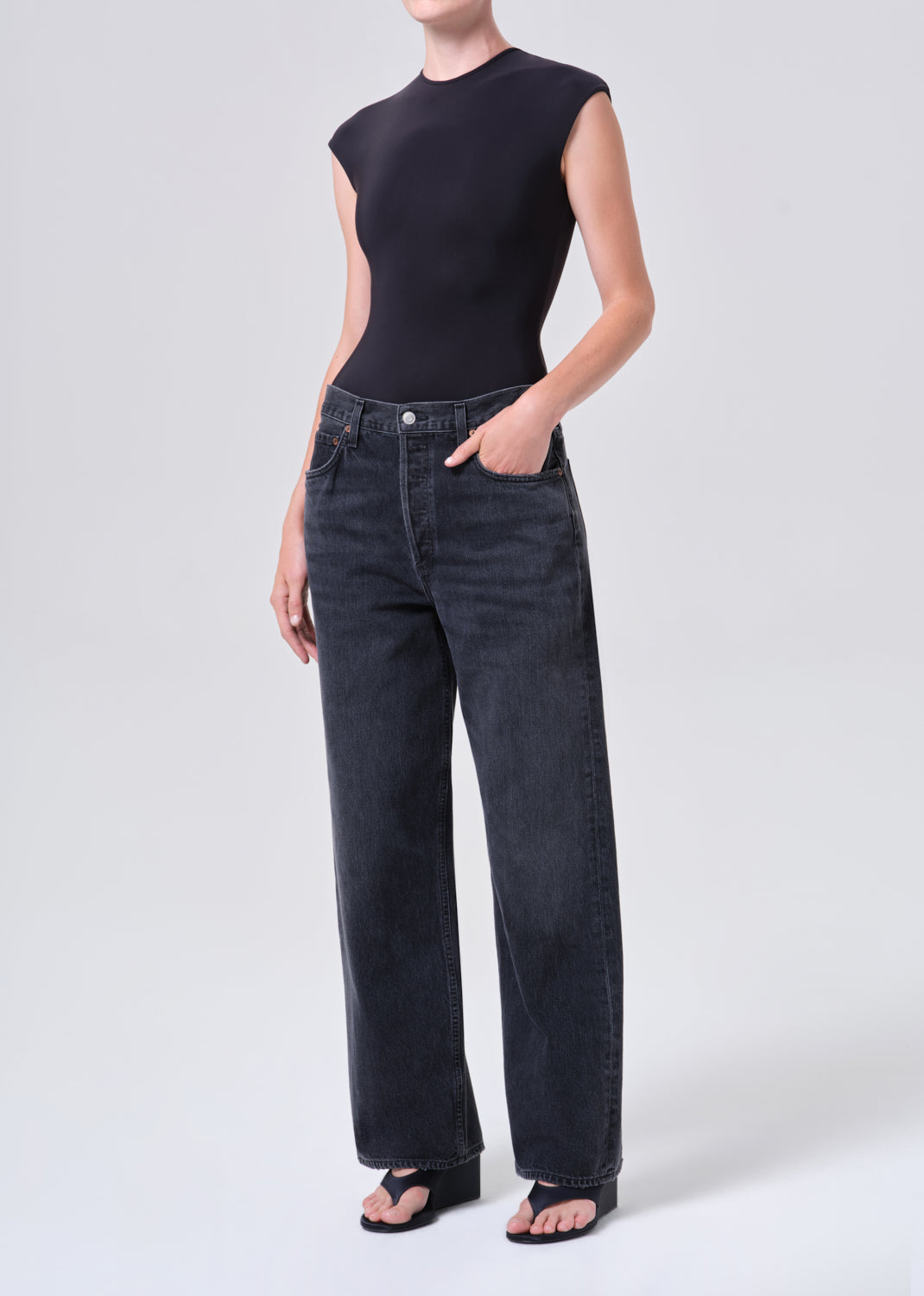 Person wearing a black sleeveless top and dark jeans on a white background