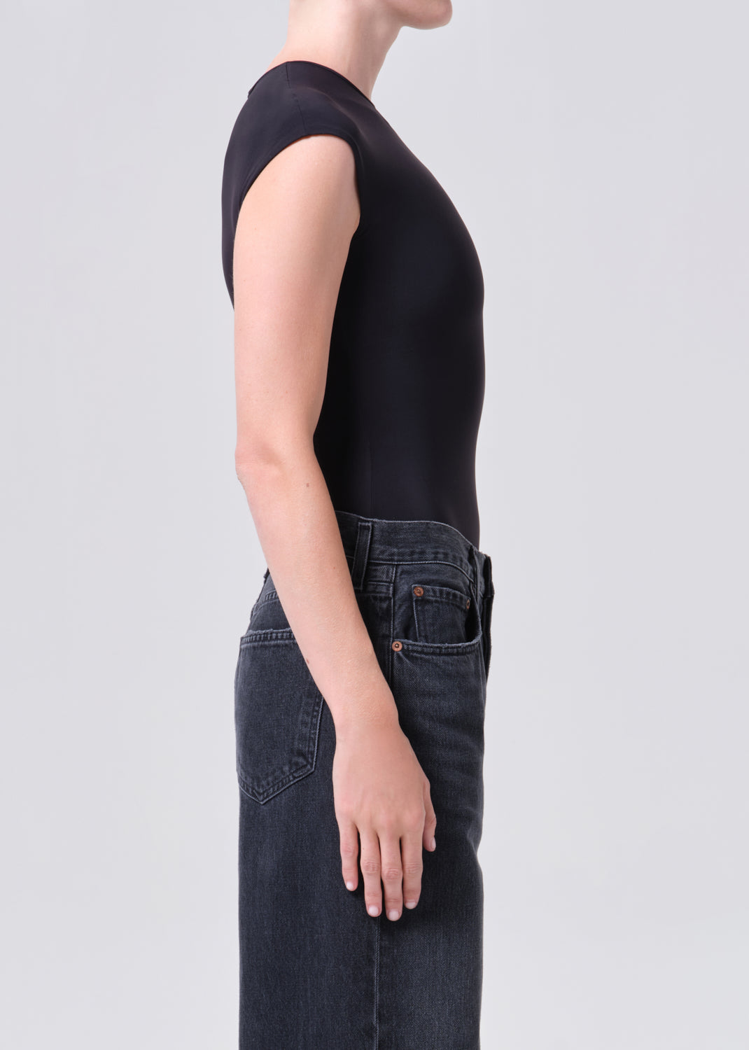 Person wearing a black sleeveless top and dark jeans on a light gray background