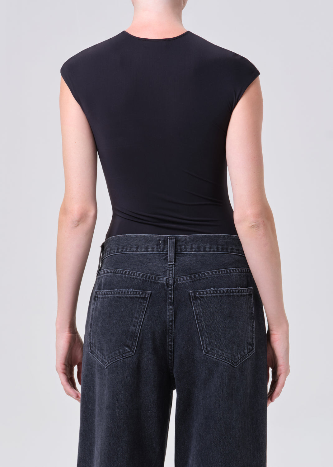 Person wearing a black sleeveless top and dark jeans on a plain background