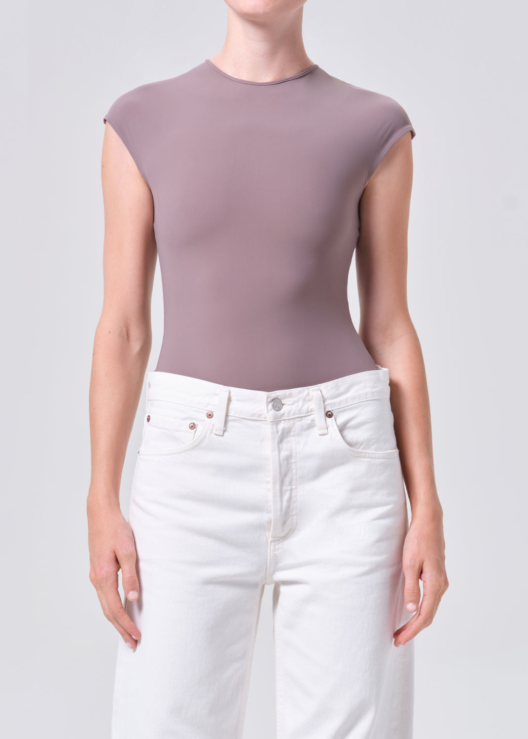 Person wearing a mauve sleeveless top and white pants on a plain background