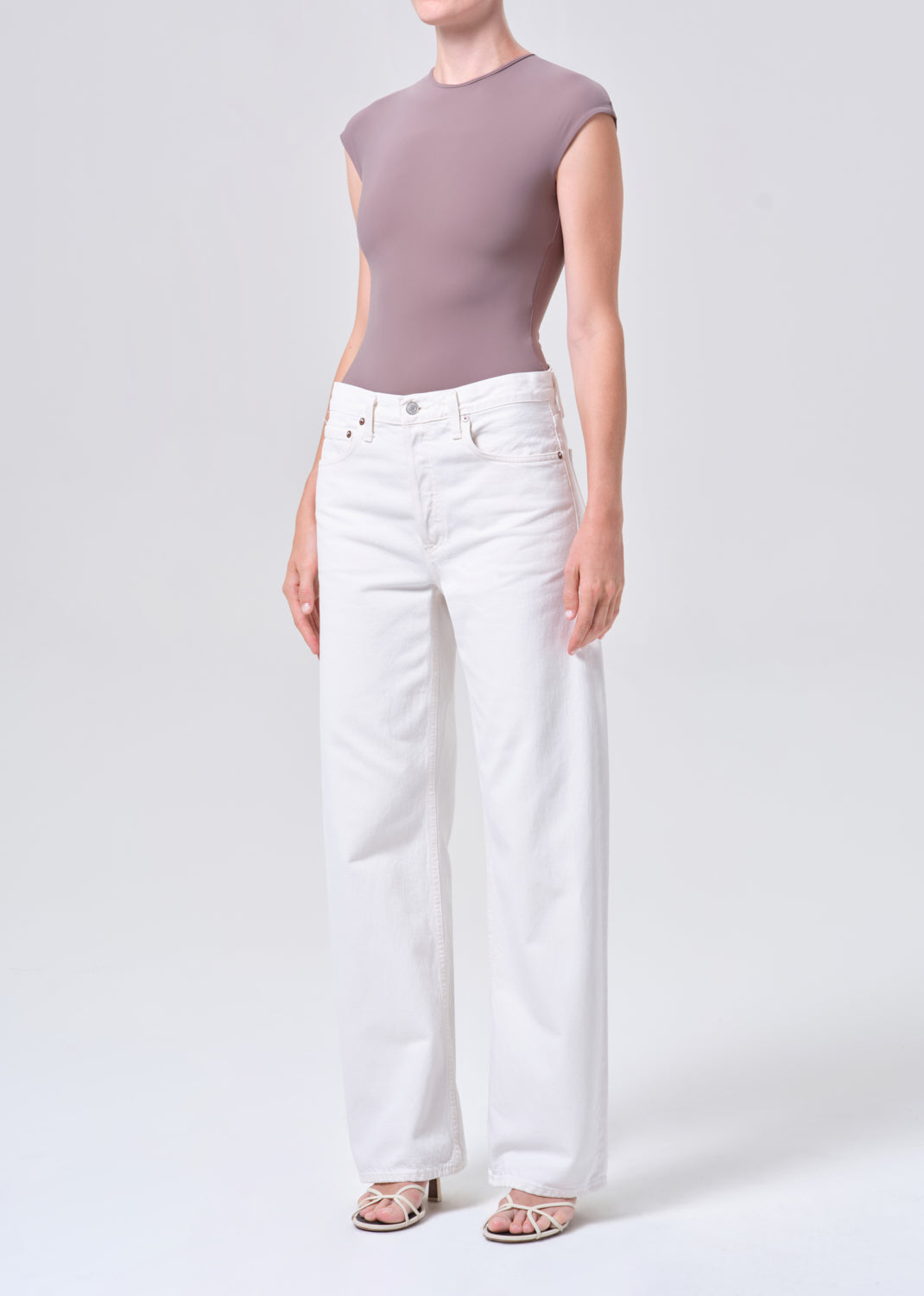 Person wearing a mauve sleeveless top and white jeans on a light gray background