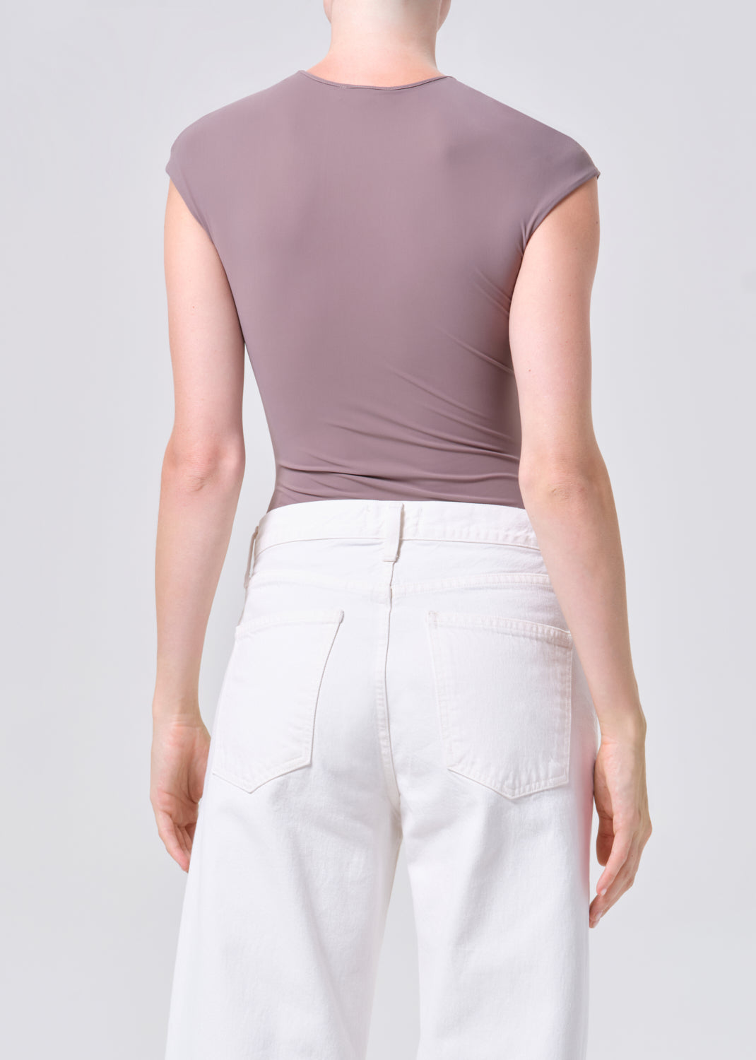 Person wearing a mauve sleeveless top and white pants on a light gray background