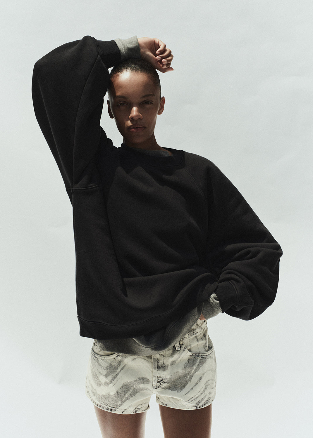 Person wearing a black oversized hoodie and light-colored shorts on a white background