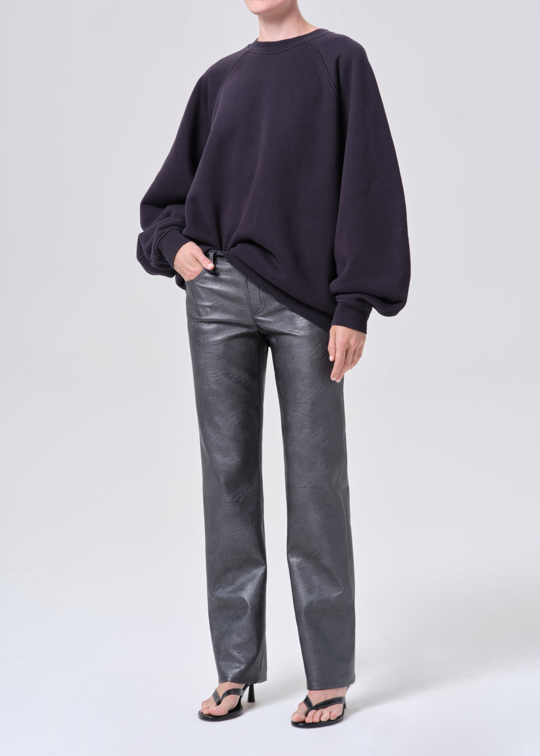 Person wearing a dark sweater and gray leather pants on a white background