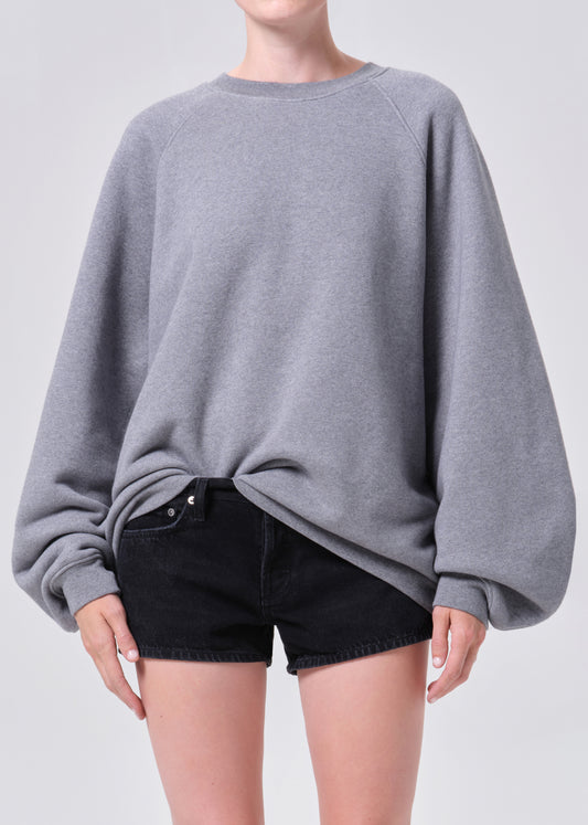 Person wearing a gray oversized sweater and black shorts on a light gray background