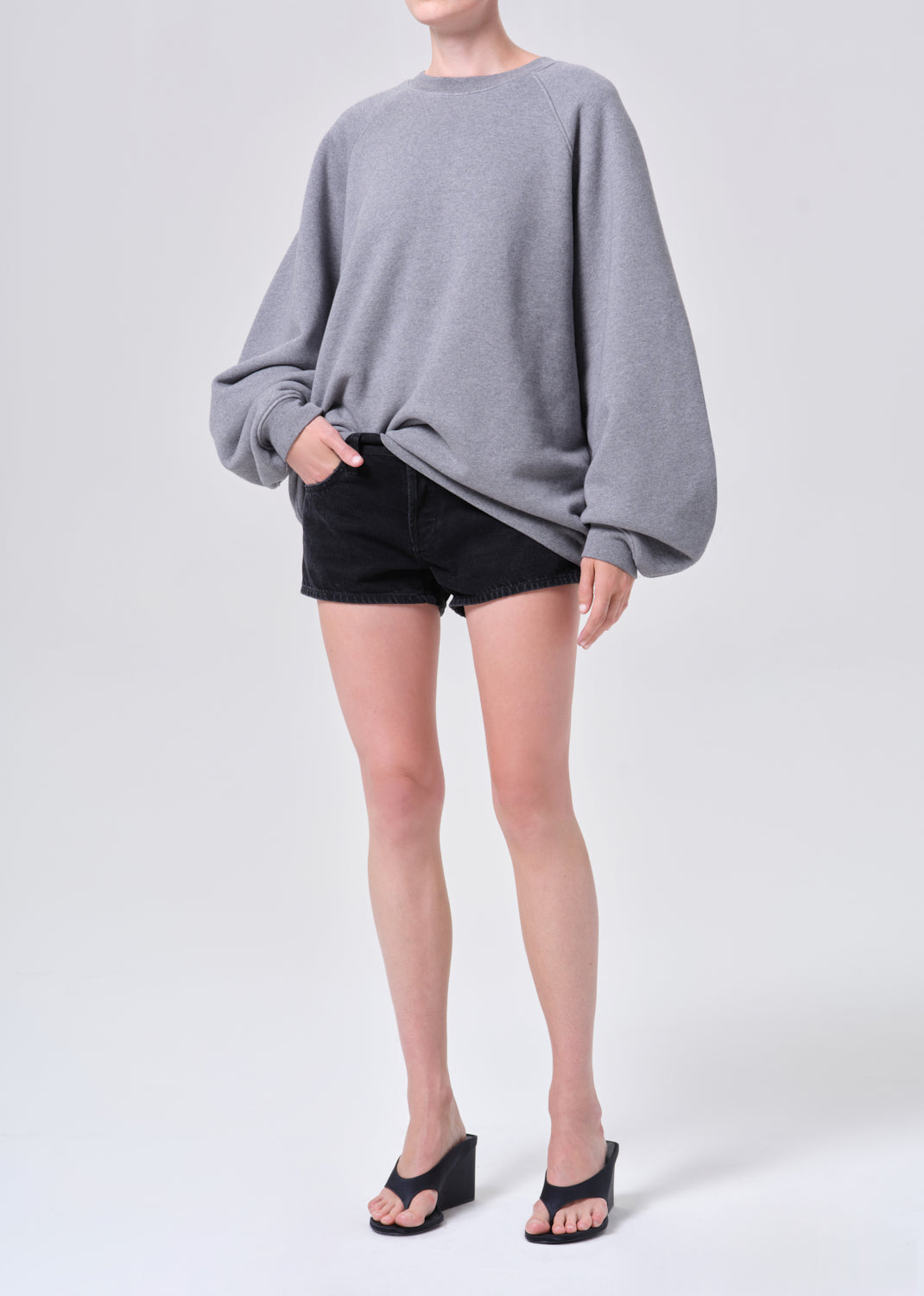 Person wearing a gray oversized sweater and black shorts on a white background