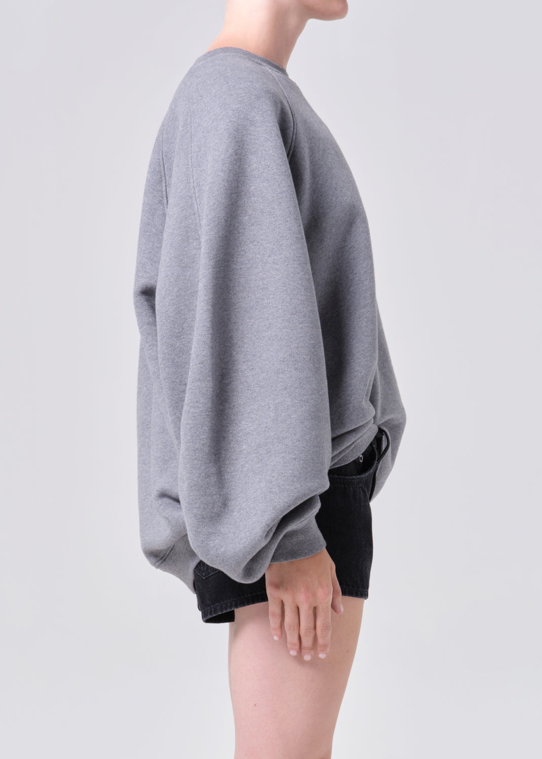 Person wearing a gray poncho over black shorts on a light gray background