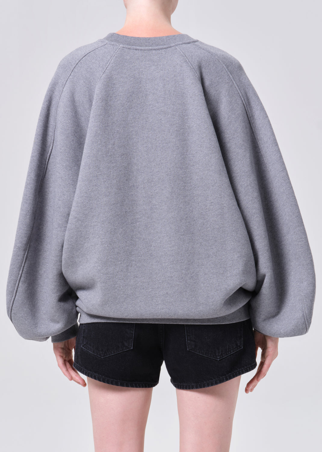 Person wearing a gray oversized sweater and black shorts on a light gray background