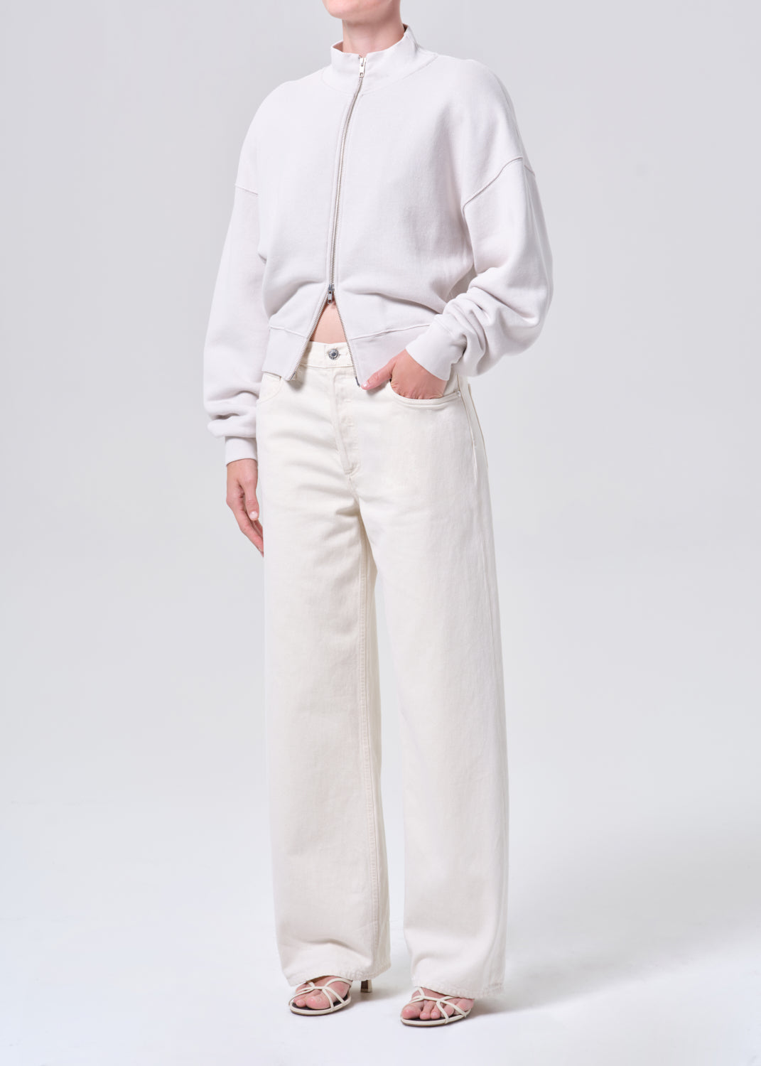 Person wearing a light gray sweater and white pants on a plain background